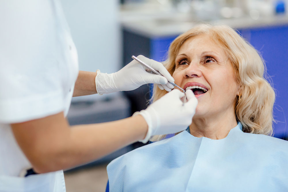 Older woman smiling during a dental exam at TrueCare Dentistry with a hygienist in gloves.