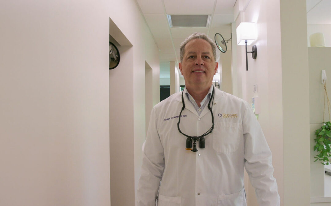 Dr. Patrick Lawrence, DDS, smiling in hallway at TrueCare Dentistry wearing white coat and loupes.